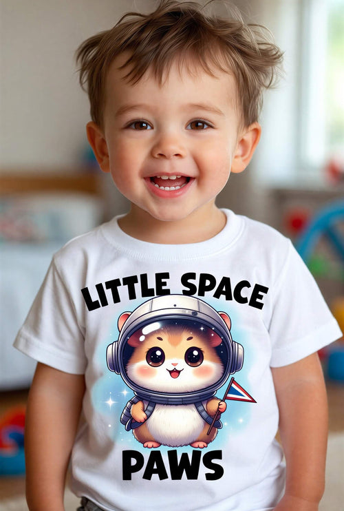 Toddler wearing a white t-shirt with a cartoon hamster in a space helmet and the text "Little Space Paws.